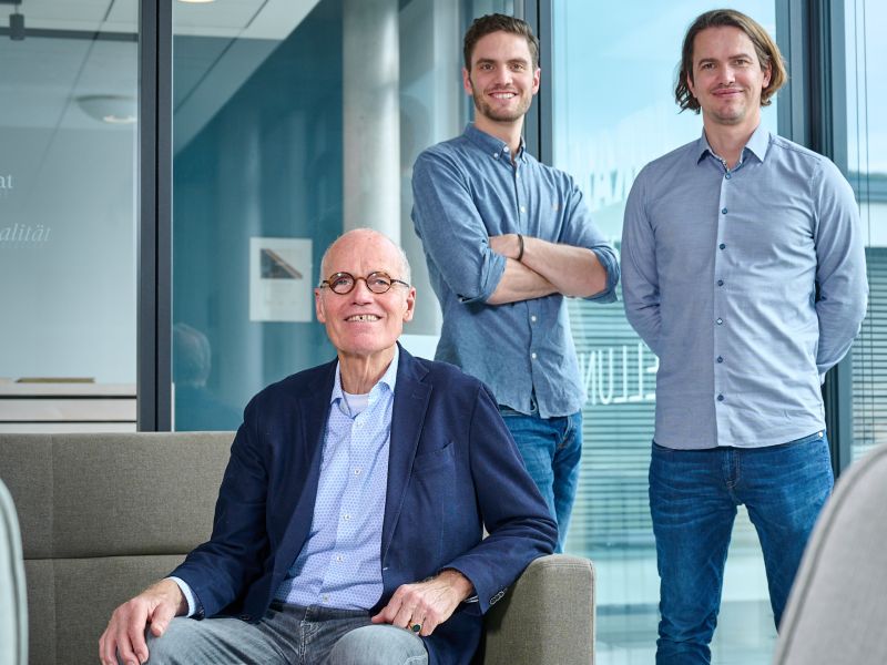 Familie von Saucken im Buro in einem modernen Buero, einer sitzt auf einem Sessel, zwei stehen dahinter vor grossen Fenstern.